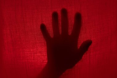 Kırmızı ışıkta perdenin arkasındaki el silueti. Cadılar Bayramı ve şiddet kavramı