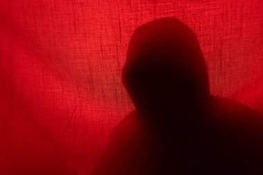 Kırmızı ışıkta perdenin arkasında bir adam silueti. Cadılar Bayramı ve şiddet kavramı