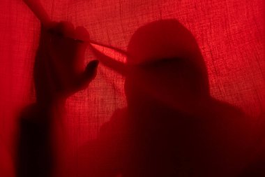 Kırmızı ışıkta perdenin arkasında bir adam silueti. Cadılar Bayramı ve şiddet kavramı