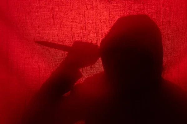 Man with a knife silhouette behind a curtain. Halloween and violence concept