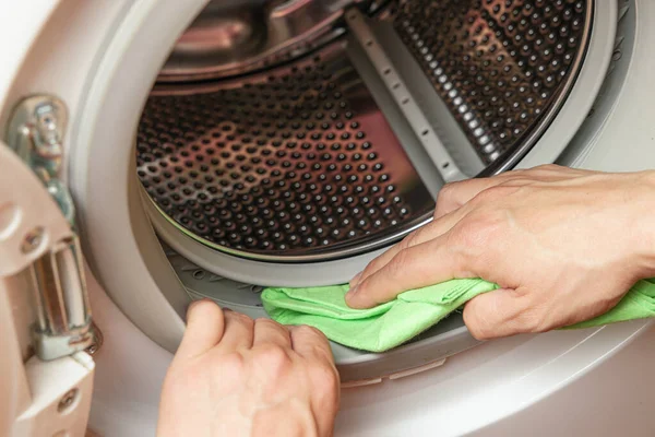 Hands cleaning moisture from the washing machine drum. Washing machine maintenance concept