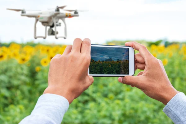 Farmer with smart phone on field with drone flying above farmland