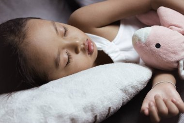 Sevimli küçük kız siyah koltukta en sevdiği oyuncakla uyuyor..