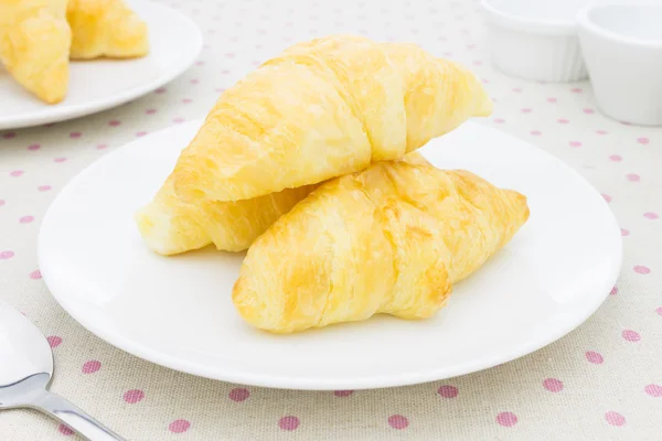 Croissant o panadería en plato blanco en mantel con cuchara y té —  Fotos de Stock