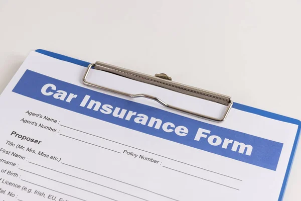 Car Insurance Claim Form or Auto Insurance Document on Right Slant and Clipboard on White Office Table