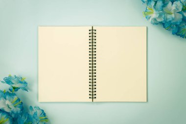 Üst Tablo Spiral Not Defteri ya da Çizgisiz Not Defteri Orta Çerçeve ve Mavi Çiçekler Üzerinde Mavi Pastel Minimalist Arkaplanda Alt Sol ve Üst Sağ Köşede