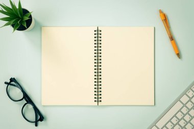 Top Table Spiral Notebook ya da Spring Notebook Center Frame ve Orange Pen ve Glasses ve Office Plant ve Klavye Mavi Pastel Minimalist Arkaplan Üzerine Çizgisiz Ton Model