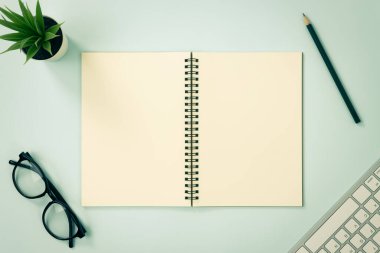 Top Table Spiral Notebook veya Spring Notebook Mockup in Unline Type on Center Frame and Pencil and Glasses and Office Plant and Klavye on Blue Pastel Minimalist Arkaplan