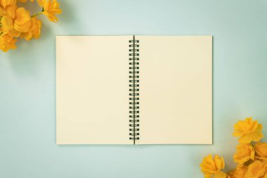 Üst Tablo Spiral Not Defteri ya da Çizgisiz Not Defteri Orta Çerçeve ve Sarı Çiçekler Üzerinde Mavi Pastel Minimalist Arkaplanda Alt Sağ ve Üst Sol Köşede