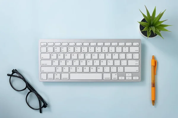 ホワイトポータブルコンピュータキーボードキーまたはキーボードボタンとブルーパステルミニマリストの背景にオレンジペンとメガネとオフィス工場を含むオフィス用品 — ストック写真