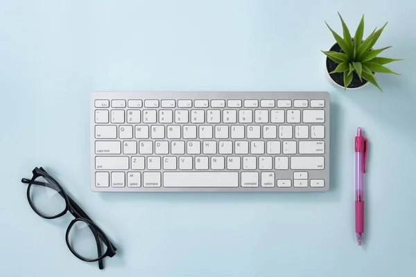 ホワイトポータブルコンピュータキーボードキーまたはキーボードボタンとブルーパステルミニマリストの背景にピンクのペンとメガネとオフィス工場を含むオフィス用品 — ストック写真