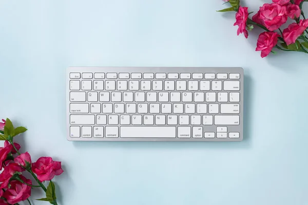 White Portable Computer Keyboard Keys or Keyboard Button and Rose Flower at Top Right and Bottom Left Corner on Blue Pastel Minimalist Background
