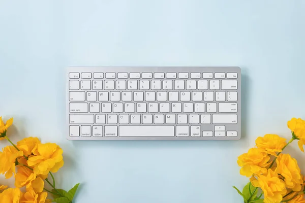 ホワイトポータブルコンピュータキーボードキーまたはキーボードボタンとブルーパステルミニマリストの背景の下に黄色の花 — ストック写真