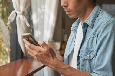 Önden Genç Asyalı Gündelik İş Adamı Denim 'de ya da Kafe' de Akıllı Telefon kullanan Kot Gömlekli. Teknoloji ile çalışan sıradan bir iş adamı
