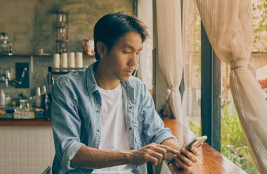 Ön Sağ Vücut Genç Asyalı Sıradan İş Adamı Denim ya da Kafe 'de Akıllı Telefon Kullanan Kot Gömlekli. Vintage Tone Teknolojisi 'nde çalışan sıradan bir iş adamı.