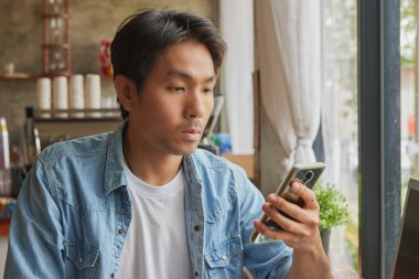 Zoom View Front Right Asyalı günlük iş adamı Denim 'de ya da Kafe' de Akıllı Telefon Kullanan Kot Gömlekli. Teknolojide Gündelik İşadamı