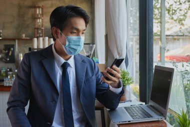 Takım Elbiseli Ön Sağ Asyalı İş Adamı Akıllı Telefon ve Kafe Sahnesinde Dizüstü bilgisayar kullanıyor. Asyalı İşadamı, Teknolojiyle Her Yerde Çalışır 19. durumda