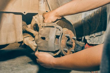 Car Mechanic Assemble Brake Caliper to Front Car Wheel Hub in Car Repair Shop in Vintage Tone