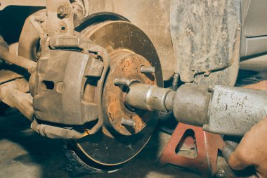 Car Mechanic Using Wind Block Tight Front Drive Shaft Nut in Car Repair Shop in Vintage Tone