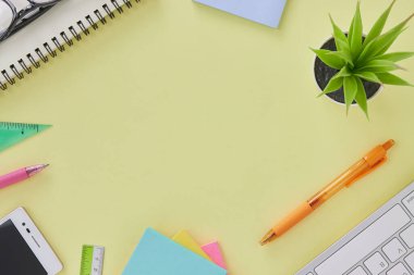 Flat Lay ya da Top View Modern Office Masası veya Klavye, Pen, Stick Nota, Cetvel, Akıllı Telefon, Not Defter, Ofis Bitkileri, Gözlüklü Ofis Masası. Sarı Minimalist Çalışma Alanı Arkaplanı