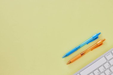 Top View veya Flat Lay Modern Office Masası veya Office Table with Computer Klavye and Blue and Orange Pen. Sarı Minimalist Çalışma Alanı Arkaplan ve Ofis Malzemeleri