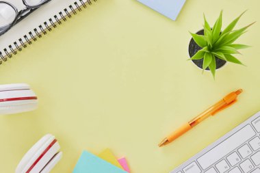 Top View ya da Flat Lay Modern Office Masası ya da Klavye, Pen, Stick Note, Kulaklık, Not Defteri, Gözlük, Ofis Bitkileri olarak Kırtasiye Masası. Sarı Minimalist Çalışma Alanı Arkaplanı