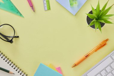 Top View veya Flat Lay Modern Ofis Masası veya Ofis Malzemeleri Klavye, Kalem, Not Defteri, Kalem, Gözlük, Cetvel, Su Seviyesi, Bitki. Sarı Minimalist Çalışma Alanı Arkaplanı