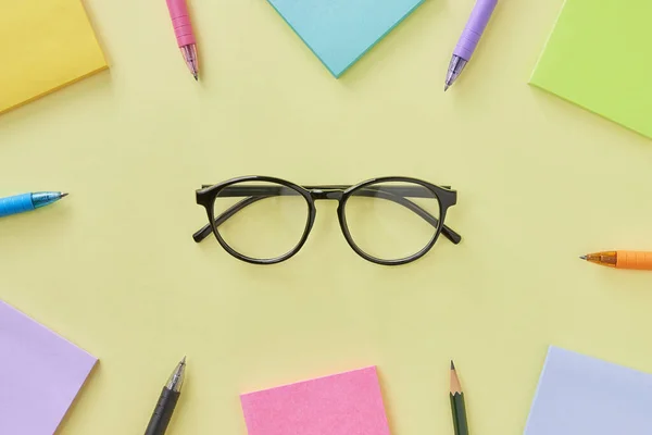 Top View or Flat Lay Glasses and Stick Note and Pen on Office Desk or Table Background. Office Supplies on Yellow Minimalist Background