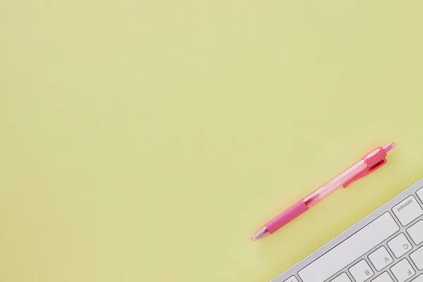 Top View or Flat Lay Modern Clean Office Desk or Office Table with Computer Keyboard and Pink Pen. Yellow Minimalist Workspace Background and Office Supplies