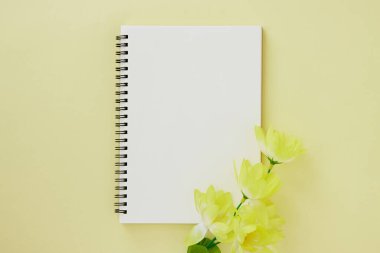 Spiral Not Defteri ya da Çizgisiz Tür ve Pastel Sarı Minimalist Arkaplan 'da Açık Sarı Çiçek ile Bahar Defteri. Spiral Not Defteri Orta Çerçeve 'ye uydur