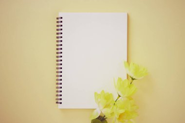 Spiral Not Defteri ya da Çizgisiz Tür ve Pastel Sarı Minimalist Arkaplan 'da Açık Sarı Çiçek ile Bahar Defteri. Spiral Not Defteri Orta Çerçeve 'ye Eski Ton' da Uygula