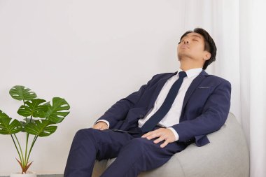 Takım Elbiseli Asyalı İşadamı ya Gözünü Dinlendir ya da İçişleri Bakanlığı 'ndaki Fasulye Torbası' nda Uyu. Gerçek hayatta iş adamının dinlenme zamanı.