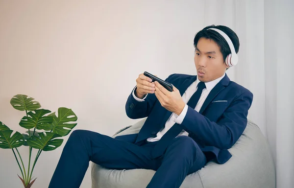 Asian Businessman in Suit Enjoy and Fun with Game Playing by Smartphone on Bean Bag at Home Office in Vintage Tone
