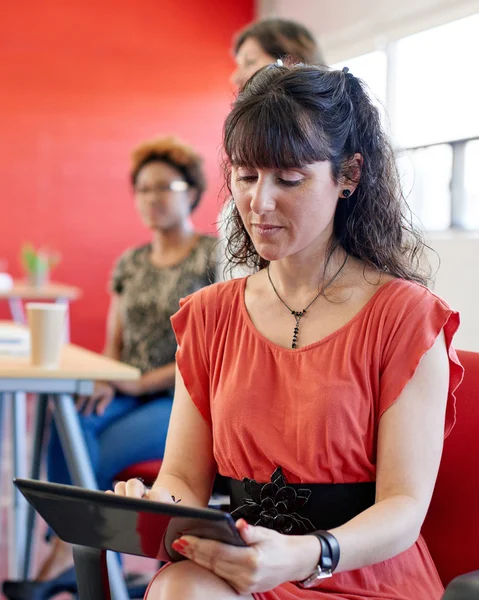 Fiduciosa designer donna che lavora su un tablet digitale in uno spazio ufficio creativo rosso — Foto Stock