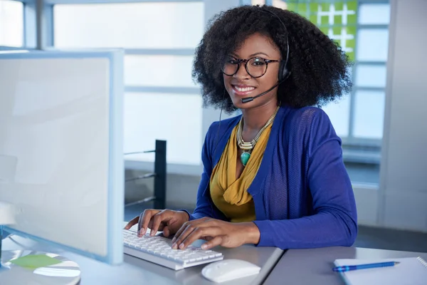 Retrato de un representante de servicio al cliente sonriente con un afro en el ordenador usando auriculares Imagen De Stock