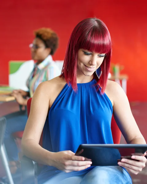 Diseñadora femenina segura trabajando en una tableta digital en un espacio de oficina rojo creativo —  Fotos de Stock