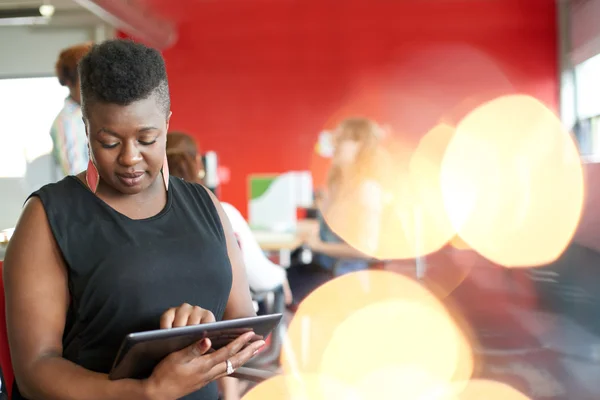 Diseñadora femenina segura trabajando en una tableta digital en un espacio de oficina rojo creativo —  Fotos de Stock