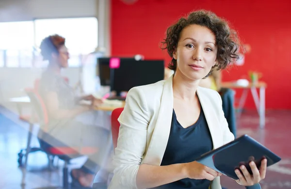 Diseñadora femenina segura trabajando en una tableta digital en un espacio de oficina rojo creativo — Foto de Stock