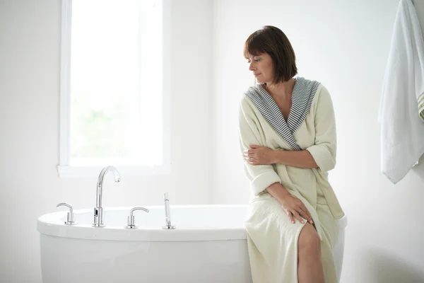 Serene mature woman sitting by a bathtub — Stock Photo, Image