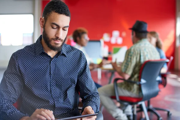 Designer masculino confiante trabalhando em um tablet digital no espaço de escritório criativo vermelho — Fotografia de Stock