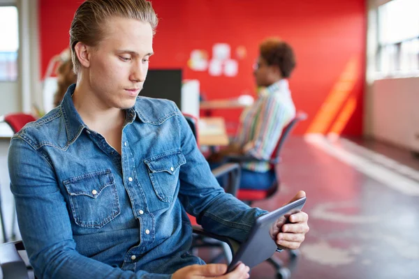 Diseñador masculino confiable trabajando en una tableta digital en el espacio de oficina creativo rojo —  Fotos de Stock