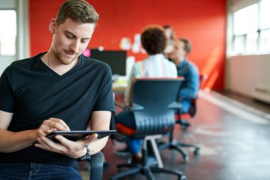 Confident male designer working on a digital tablet in red creative office space clipart