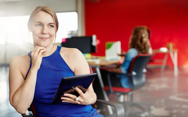Diseñadora femenina segura trabajando en una tableta digital en un espacio de oficina rojo creativo — Foto de Stock
