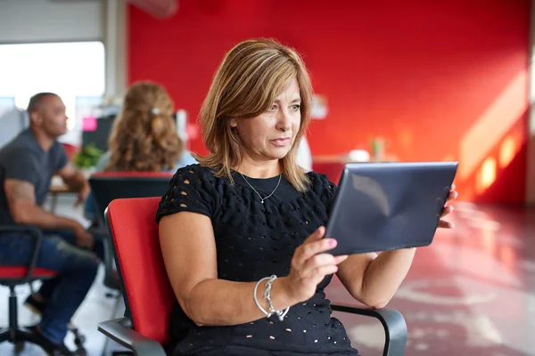 Diseñadora femenina segura trabajando en una tableta digital en un espacio de oficina rojo creativo —  Fotos de Stock