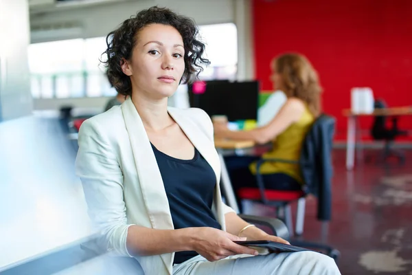 Diseñadora femenina segura trabajando en una tableta digital en un espacio de oficina rojo creativo — Foto de Stock