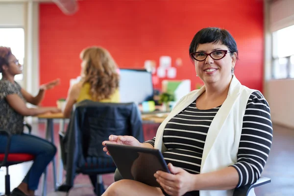 Diseñadora femenina segura trabajando en una tableta digital en un espacio de oficina rojo creativo — Foto de Stock