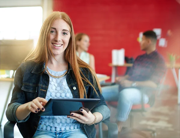 Confiada pelirroja diseñadora femenina trabajando en una tableta digital en rojo creativo espacio de oficina — Foto de Stock