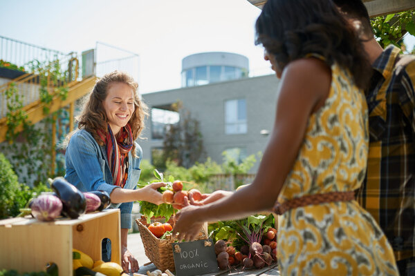Friendly woman tending an organic vegetable stall at a farmers market and selling fresh vegetables from the rooftop garden