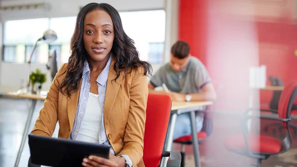 Diseñadora femenina segura trabajando en una tableta digital en un espacio de oficina rojo creativo — Foto de Stock