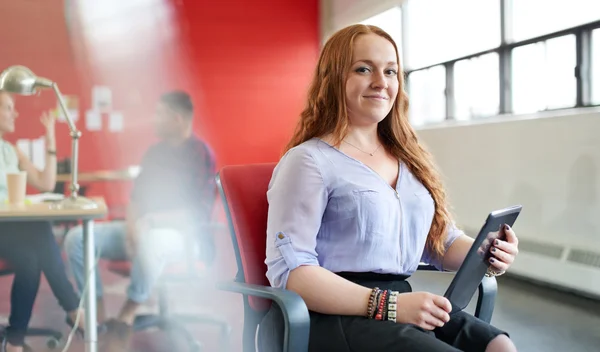 Confiada pelirroja diseñadora femenina trabajando en una tableta digital en rojo creativo espacio de oficina —  Fotos de Stock